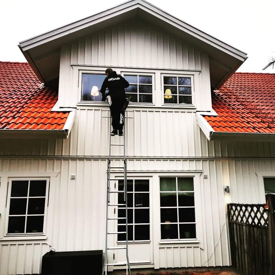 En anställd på GÖAB putsar utsidan av fönster på en villa.