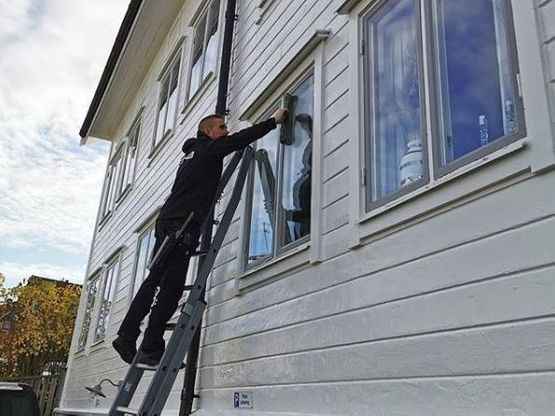 En anställd på GÖAB står på en stege och putsar utsidan av ett fönster på ett större hus.