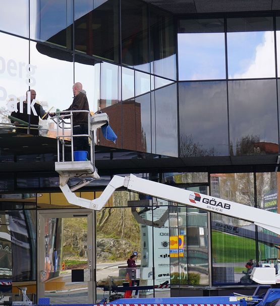 En anställd på GÖAB står i en skylift och putsar stora fönsterpartier på en större kontorsbyggnad i Göteborg.